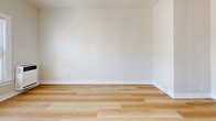 Located at 919 S Manhattan Place in the Mid-City neighborhood of Los Angeles, this single-floor, one-bedroom, one-bathroom unit offers an efficient and thoughtfully arranged layout. Light-toned hardwood flooring runs throughout the space, creating a cohesive, clean aesthetic across every room.

The bedroom is a generously proportioned room for a unit of this scale, occupying roughly half of the total floor area. A pair of double-hung windows with blinds fills the room with natural light and offers views of the surrounding neighborhood's greenery and rooftops. A wall-mounted heater ensures comfort year-round.

The kitchen features a galley-style configuration with white shaker cabinetry — both upper and lower — paired with a marble-pattern countertop and a stainless steel sink. The white-on-white palette keeps the space feeling bright and open despite its compact footprint.

A hallway connects the main living areas and provides access to the bathroom, which includes a stand-up shower stall finished in white subway tile with a classic black-and-white octagonal mosaic tile floor — a timeless detail that adds character. The overall ambiance of the unit is clean, minimal, and move-in ready, making it a practical option in the heart of Los Angeles.