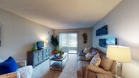 This single-floor residence offers a thoughtfully organized layout encompassing a living room, dining area, kitchen, and bedroom. The living room serves as the central gathering space, featuring wall-to-wall carpet, a textured ceiling, and a sliding glass door that opens to a balcony, allowing natural light to filter in and providing outdoor views. The room accommodates generous seating and media storage, creating a comfortable and functional environment.

Adjacent to the living area, the dining space features wood-style flooring, a track lighting fixture overhead, and room for a full dining set. A barn-style sliding door adds a practical design detail connecting to nearby spaces.

The galley-style kitchen is efficiently arranged with white cabinetry extending to the ceiling, white appliances including a coil-burner range and refrigerator, and the same wood-style flooring carried throughout the area. The layout maximizes storage and workspace within a compact footprint.

The bedroom is a calm, carpeted retreat with a textured ceiling and neutral walls. It comfortably fits a full-sized bed with flanking nightstands and offers ample space for a large dresser. The room connects to the rest of the unit through a hallway, contributing to a clear and practical flow throughout the residence.
