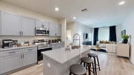 This single-floor residence is designed with a contemporary aesthetic, combining functionality and style throughout its open layout. The kitchen serves as a central hub, featuring gray shaker-style cabinetry, granite countertops, and a full suite of stainless steel appliances, including a French door refrigerator, electric range with microwave above, and a large center island with seating for casual dining. Light wood-tone flooring runs throughout the main living areas, enhancing the bright, airy feel of the space.

The kitchen flows seamlessly into the living room, which is bathed in natural light from multiple windows dressed with blinds and dark curtain panels. The bedroom offers a quieter retreat, with soft carpeting and direct access to a spacious walk-in closet equipped with built-in shelving and hanging rods. The en-suite bathroom features a granite-topped vanity with gray cabinetry, wood-tone flooring, and a full soaking tub enclosed by classic white subway tile. A dedicated in-unit laundry area with a top-load washer adds everyday convenience, completing this well-organized and thoughtfully designed residence.
