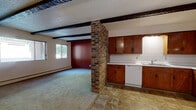 Located in Sartell, Minnesota, this single-floor, three-bedroom, one-bathroom residence offers a practical and character-rich layout. The open living area makes a strong first impression with its textured ceiling, dark exposed wood beams, and a prominent brick accent column that visually separates the living space from the kitchen. Natural light filters in through windows overlooking mature trees, and baseboard heating runs throughout the home. The kitchen is well-equipped with warm oak cabinetry extending along multiple walls, white tile backsplash, stone-look tile flooring, and white appliances including a range, dishwasher, and refrigerator. A wood-paneled wainscoting detail adds a classic touch near the entryway. The three bedrooms are carpeted and simply appointed, each featuring baseboard heating. The spacious primary bedroom includes a wide double closet with built-in rods and shelving. The additional bedrooms each offer windows with views of the surrounding greenery. The full bathroom features a wood-framed vanity with a marble-patterned countertop, a large mirror, tile wainscoting, and classic mosaic tile flooring. A central hallway connects the bedrooms and bathroom, providing a functional flow throughout this cozy Sartell home.