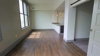Located at 8 E Long St in the heart of Columbus, Ohio, this single-floor unit offers a contemporary open-concept design that seamlessly blends the living and kitchen areas. Rich hardwood-style flooring flows throughout the main living space, complemented by clean white walls and large windows that invite an abundance of natural light, creating a bright and welcoming atmosphere.

The kitchen is a standout feature, showcasing an expansive granite countertop island that doubles as a breakfast bar, providing both prep space and casual dining. Dark espresso cabinetry offers generous storage and creates a striking contrast against the light granite surfaces. A full suite of stainless steel appliances — including a refrigerator with ice maker, electric range, built-in microwave, and dishwasher — ensures a fully equipped cooking experience. Stylish pendant lighting hangs above the island, adding a warm, modern touch to the space.

The open living area is generously proportioned, offering flexible furniture arrangements and a comfortable flow from the kitchen. A barn-style sliding door adds a modern industrial accent, while recessed lighting throughout enhances the overall ambiance. The unit presents a polished, move-in ready interior well-suited for urban living in downtown Columbus.