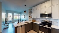 This thoughtfully designed single-floor residence offers a cohesive blend of modern aesthetics and functional living. The open-concept kitchen is a standout feature, equipped with stainless steel appliances including a range, over-the-range microwave, dishwasher, and refrigerator. Two-toned cabinetry pairs dark lower cabinets with crisp white upper cabinets, complemented by white subway tile backsplash and light quartz countertops. A peninsula with an undermount sink adds both workspace and a casual dining option, while a pendant light adds a stylish focal point overhead.

The living area flows naturally from the kitchen and is bathed in natural light from large windows and a glass door that opens to a private balcony, offering urban views of the surrounding cityscape. Light hardwood-style flooring runs throughout, contributing to the bright and airy atmosphere.

The bedroom is a calm retreat featuring a large picture window with sweeping city views, soft neutral walls, and the same warm flooring found throughout the unit. A full bathroom with a wide vanity, undermount sink, and clean white finishes provides a polished, spa-like feel.

A dedicated laundry area with stacked washer and dryer units, along with built-in shelving for additional storage, rounds out the practical amenities of this well-appointed space.