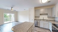 Located at 2778 Second Street Northeast in Hickory, NC, this well-appointed one-bedroom, one-bathroom residence offers a thoughtfully designed layout across a single floor. The entrance leads into a bright, open living area featuring hardwood-style flooring, crown molding, and a ceiling fan with a gold-toned fixture. A sliding glass door opens to a private balcony, offering pleasant views of lush greenery and the surrounding landscape.

The kitchen is a standout feature, equipped with grey shaker-style cabinetry, granite countertops, a center island for additional prep space, and a full suite of stainless steel appliances including a refrigerator, electric range, and microwave. Pendant lighting and wood-look flooring complete the contemporary aesthetic.

The bedroom is carpeted for comfort and includes a ceiling fan, a closet, and a window that brings in natural light. The full bathroom is finished with a granite-topped vanity, white cabinetry, wood-look flooring, and a tub-shower combination.

A dedicated laundry room houses a full-size washer and dryer alongside overhead shelving for added storage. The hallway connects all rooms efficiently, contributing to the unit's functional and comfortable flow throughout.
