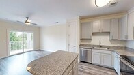 Located at 2778 Second Street Northeast in Hickory, NC, this well-appointed one-bedroom, one-bathroom residence offers a thoughtfully designed layout across a single floor. The entrance leads into a bright, open living area featuring hardwood-style flooring, crown molding, and a ceiling fan with a gold-toned fixture. A sliding glass door opens to a private balcony, offering pleasant views of lush greenery and the surrounding landscape.

The kitchen is a standout feature, equipped with grey shaker-style cabinetry, granite countertops, a center island for additional prep space, and a full suite of stainless steel appliances including a refrigerator, electric range, and microwave. Pendant lighting and wood-look flooring complete the contemporary aesthetic.

The bedroom is carpeted for comfort and includes a ceiling fan, a closet, and a window that brings in natural light. The full bathroom is finished with a granite-topped vanity, white cabinetry, wood-look flooring, and a tub-shower combination.

A dedicated laundry room houses a full-size washer and dryer alongside overhead shelving for added storage. The hallway connects all rooms efficiently, contributing to the unit's functional and comfortable flow throughout.