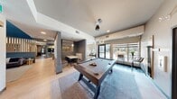 Located in Calgary, AB, this thoughtfully designed social lounge offers a generous, open-concept layout across a single floor. The space is defined by a modern aesthetic, combining warm wood tones, cool grey walls with deep teal accents, and light hardwood-style flooring throughout.

At the heart of the lounge is a striking full-height stacked stone fireplace wall, complete with a linear electric fireplace and a wall-mounted television, flanked by comfortable sofas — a natural gathering point for residents. Adjacent to this seating area, vertical wood slat partitions serve as elegant room dividers, separating zones while maintaining an open, airy feel.

The game area features a solid wood pool table set beneath contemporary pendant lighting, including a distinctive circular ring fixture. Nearby, a built-in banquette dining nook provides an intimate space for casual meals or conversation. A dedicated Starbucks coffee station adds a premium amenity touch, while a corridor lined with curated artwork, including a large-scale Calgary cityscape photograph, connects the various zones.

Floor-to-ceiling windows and glass doors flood the space with natural light and provide direct access to an outdoor patio area. The lounge's cohesive design, combining stylish furnishings, warm lighting, and premium finishes, creates a welcoming, versatile environment suited for both relaxation and social engagement.