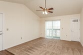 This single-floor residence offers a well-organized layout with a seamless flow between its main living areas. The living room is a standout space, distinguished by soaring vaulted ceilings and a ceiling fan with integrated lighting that enhances the sense of openness. Plush carpet covers the living and bedroom areas, while wood-look hard flooring extends through the kitchen and entryway zones. A sliding glass door fitted with vertical blinds fills the living room with natural light and provides direct access to an outdoor area.

The kitchen is positioned adjacent to the living space and separated by a raised breakfast bar with a wood-toned countertop, creating an open yet defined boundary. Warm oak cabinetry lines the kitchen walls, offering generous storage, while laminate countertops and a white electric coil-burner range with overhead exhaust hood provide functional cooking amenities. A white refrigerator completes the appliance suite.

The bedroom features its own ceiling fan, a standard window with blinds inviting natural light, and soft carpet underfoot. The bathroom is finished with tile flooring, an oak vanity with a stone-toned countertop, a framed mirror, and a full tub-shower combination unit with built-in shelving. A laundry area is also present within the unit.