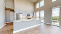This thoughtfully designed 2-bedroom, 2-bathroom residence offers a seamless blend of modern finishes and functional living spaces across a single floor. The open-concept kitchen and living area is the heart of the home, boasting dramatic double-height ceilings and floor-to-ceiling windows that flood the space with natural light and provide sweeping outdoor views. The kitchen is appointed with sleek gray cabinetry, a classic subway tile backsplash, white quartz countertops, a large center island, and a full suite of stainless steel appliances. Light wood-style flooring runs throughout the main living areas, enhancing the bright and airy atmosphere. The spacious living room opens directly onto a private balcony through sliding glass doors, extending the living space outdoors. Both bedrooms are carpeted for comfort, with the primary bedroom featuring its own balcony access, a ceiling fan, and a generous walk-in closet with built-in shelving and hanging rods. The two bathrooms are finished with gray vanity cabinetry, light tile flooring, and modern fixtures. A hallway with built-in shelving provides additional storage, connecting the living and sleeping areas with ease. The overall aesthetic is clean, contemporary, and move-in ready.