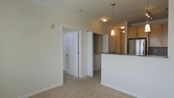 This single-floor residence offers a clean, functional layout designed for comfortable everyday living. The open-concept living and dining area is finished with plush neutral carpeting and crisp white walls, creating a bright and welcoming atmosphere. Crown molding adds a refined architectural detail throughout the space.

The kitchen is positioned adjacent to the living area, separated by a raised breakfast bar countertop with granite-style stone surfaces. Pendant lighting hangs above the bar, casting a warm glow over the space. The kitchen is equipped with stainless steel appliances and features warm wood-toned cabinetry, providing ample storage. Recessed and flush-mount ceiling lights ensure the kitchen remains well-lit.

A dedicated laundry closet is conveniently located off the main living space, housing a stacked or side-by-side washer and dryer unit behind louvered doors — a practical in-unit amenity. Additional doors off the main hallway lead to further rooms within the residence, including what appears to be a closet or utility area with built-in shelving.

White six-panel interior doors, clean baseboards, and a consistent neutral color palette throughout give the space a cohesive and well-maintained appearance, making it move-in ready and easy to personalize.