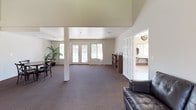 Located at 532 Broadway in El Cajon, California, this single-story community facility offers a well-organized and functional layout designed to serve its occupants with comfort and convenience. The space is characterized by clean white walls, neutral carpeting, and an open, airy feel throughout.

The lounge area makes a strong impression with its dramatic vaulted ceiling accented by exposed beams, creating a sense of generous vertical space. Two large leather sofas face each other around a central coffee table, while a window allows natural light to fill the room — making it an inviting setting for relaxation or casual gatherings.

Adjacent to the lounge is a spacious open gathering room, supported by a structural column and featuring tall ceilings that add to the sense of openness. French doors lead to an exterior view, and a bookcase along one wall provides additional functionality. A smaller dining nook with a round table and cross-back chairs sits nearby, offering a comfortable spot for smaller group interactions. Greenery in the form of potted tropical plants adds a touch of warmth and life to these areas.

The laundry facility is bright and efficiently designed, with vaulted ceilings, large windows on multiple sides, and a full row of washers and dryers arranged along a central counter. Tile flooring, a utility sink, and ample natural light make this a practical and pleasant workspace.