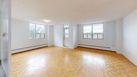 Located at 30 Carabob Ct in Toronto's Scarborough district, this single-floor, two-bedroom, one-bathroom unit offers a well-organized layout across a comfortable footprint. The living area is notably spacious, featuring warm parquet flooring in a classic herringbone pattern and multiple windows that invite generous natural light and outdoor views of the surrounding neighbourhood. Baseboard heating runs along the perimeter walls throughout, ensuring consistent warmth. The kitchen is finished with crisp white cabinetry, a white subway tile backsplash, light countertops, and white tile flooring. It is equipped with stainless steel appliances, including a range, microwave, and dishwasher, providing a functional and clean aesthetic. An adjacent area offers additional open space suitable for dining. The primary bedroom is a well-proportioned room with a large sliding mirrored closet and parquet flooring, while the second bedroom also features parquet floors and a window with outdoor views. The bathroom includes a full soaker tub with an overhead shower, framed by white horizontal subway tile surround. Throughout the unit, white walls and clean finishes create a bright, neutral ambiance.