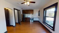 Located at 304 W Touhy Ave in Park Ridge, Illinois, this single-floor unit offers a practical and well-appointed layout with consistent design details throughout. The main living area features warm hardwood flooring and a ceiling fan with integrated lighting, creating a comfortable and functional space. The kitchen is positioned within the open-plan main room and is equipped with rich dark wood cabinetry, a classic white subway tile backsplash, light stone-toned countertops, a stainless steel sink, a gas range with oven, and a full-size black refrigerator. A range hood is installed above the stove, and a window provides natural light to the kitchen area.

A charming arched doorway leads toward additional rooms, maintaining a subtle architectural character throughout the unit. The bathroom is clean and simply appointed, featuring a white vanity with an oval mirror, a toilet, and light marble-style tile flooring. Adjacent to the bathroom, a closet with built-in shelving provides convenient storage.

The bedroom is a bright, generously sized room with two large dark-trimmed windows offering views of the surrounding neighborhood greenery, allowing ample natural light to fill the space. A ceiling fan is also present here. Bold dark door and baseboard trim contrasts with the light walls throughout, adding a cohesive and intentional design touch across the unit.