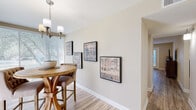 This single-floor residence on Randolph Road in North Little Rock, Arkansas, offers a thoughtfully designed layout with a warm, neutral color palette throughout. The living room serves as a central gathering space, featuring wood-look flooring, a ceiling fan, and decorative wall accents that lend a stylish, curated ambiance. Adjacent to the living area, the dining space is bathed in natural light from large windows dressed with horizontal blinds, and is anchored by a solid wood round pedestal table beneath a modern multi-bulb chandelier. The kitchen is equipped with rich wood cabinetry, granite-style countertops, and standard appliances, offering a functional and attractive workspace. The primary bedroom includes plush carpeting, dual closets, a ceiling fan, and a window that invites natural light. A secondary bedroom also features carpet flooring, a ceiling fan, and a window with outdoor views. The bathroom presents a vanity with granite-style countertops, warm wood cabinetry, wood-look flooring, and a shower-tub combination. Throughout the space, consistent finishes and tasteful design choices create a cohesive, comfortable living environment.