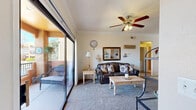 This single-floor residence offers a thoughtful layout with 2 bedrooms, 2 bathrooms, 2 closets, and a combined kitchen and living area, all connected by a central hallway. The living room is a welcoming space finished with plush carpet, crown molding, and a ceiling fan with integrated lighting. Large sliding glass doors flood the room with natural light and open onto a private balcony, offering pleasant outdoor views of surrounding landscaping and architecture. The kitchen is well-equipped with stainless steel appliances — including a gas range, built-in microwave, and refrigerator — complemented by dark granite countertops, light wood cabinetry, and hexagonal tile flooring. A dining area with recessed lighting sits adjacent to the kitchen. The primary bedroom is a comfortable, carpeted retreat with a large window dressed in decorative valance treatments, allowing ample natural light. The second bedroom mirrors this bright, carpeted aesthetic. Both bathrooms share consistent finishes, featuring dark granite countertops, light wood vanity cabinetry, hexagonal tile flooring, and a tub-shower combination. The space presents a cohesive and functional design throughout.