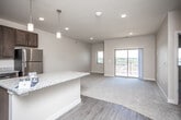 This single-floor residence offers a thoughtfully designed open-concept layout that seamlessly connects the kitchen, dining, and living areas. The kitchen serves as the heart of the home, showcasing rich dark-brown cabinetry, granite countertops, a central island with pendant lighting overhead, and a full suite of stainless steel appliances including a refrigerator, range, microwave, and dishwasher. Durable hardwood-style flooring runs throughout the kitchen and main living areas, transitioning to plush carpeting in the living room and bedroom.

The generously sized living area is filled with natural light from a large sliding glass door that opens onto a private balcony, offering open outdoor views of the surrounding landscape. An additional window provides further light and ventilation.

The bedroom is a comfortable retreat featuring a ceiling fan with light fixture, a large window with exterior views, and direct access to a spacious walk-in closet outfitted with wire shelving systems for organized storage.

The full bathroom is clean and functional, featuring a tub-shower combination, a toilet, wood-style flooring, and a vanity with granite countertops and dark cabinetry consistent with the kitchen's design aesthetic. The overall palette of neutral tones and modern finishes creates a cohesive and inviting atmosphere throughout the space.