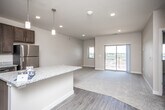 This single-floor residence offers a thoughtfully designed open-concept layout that seamlessly connects the kitchen, dining, and living areas. The kitchen serves as the heart of the home, showcasing rich dark-brown cabinetry, granite countertops, a central island with pendant lighting overhead, and a full suite of stainless steel appliances including a refrigerator, range, microwave, and dishwasher. Durable hardwood-style flooring runs throughout the kitchen and main living areas, transitioning to plush carpeting in the living room and bedroom.

The generously sized living area is filled with natural light from a large sliding glass door that opens onto a private balcony, offering open outdoor views of the surrounding landscape. An additional window provides further light and ventilation.

The bedroom is a comfortable retreat featuring a ceiling fan with light fixture, a large window with exterior views, and direct access to a spacious walk-in closet outfitted with wire shelving systems for organized storage.

The full bathroom is clean and functional, featuring a tub-shower combination, a toilet, wood-style flooring, and a vanity with granite countertops and dark cabinetry consistent with the kitchen's design aesthetic. The overall palette of neutral tones and modern finishes creates a cohesive and inviting atmosphere throughout the space.