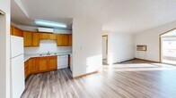 This single-floor unit offers a practical and functional layout designed for comfortable everyday living. The open-concept kitchen flows seamlessly into the living and dining areas, creating a connected and spacious feel. The kitchen features warm oak cabinetry, white appliances including a dishwasher, and a built-in sink, all illuminated by overhead fluorescent lighting. Wood-look laminate flooring runs throughout the main living spaces, adding a clean and cohesive aesthetic.

The living area is a standout feature, boasting vaulted ceilings and a large angled sliding glass door that floods the room with natural light and provides direct access to a private outdoor balcony. A wall-mounted air conditioning unit and baseboard heating ensure year-round climate comfort.

The bedroom is carpeted for warmth and comfort, features a window with exterior views, and includes a spacious double-door closet with built-in shelving and hanging rods. Two bathrooms serve the unit — one full bathroom with a single-sink vanity, large mirror, and baseboard heater, and a second bathroom equipped with a standalone shower stall, toilet, and additional wire shelving for storage. Textured ceilings are present throughout the unit.