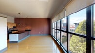 This single-floor unit showcases a thoughtfully designed open layout that seamlessly connects the main living area and kitchen. The living space is immediately striking, featuring an expansive wall of floor-to-ceiling windows fitted with roller shades, flooding the interior with natural light and offering elevated views of the surrounding urban streetscape and treetops. Light hardwood flooring runs throughout, complementing the warm terracotta-toned accent walls that lend the space a modern yet inviting character.

The kitchen is well-appointed with light maple cabinetry, dark granite countertops, a tile backsplash, and stainless steel appliances including a refrigerator, dishwasher, and built-in microwave. A peninsula with an integrated cooktop and matching granite surface extends into the living area, creating a natural gathering point and defining the kitchen zone. Pendant lighting hangs above both the peninsula and the main living area, adding architectural interest.

The bathroom is cleanly finished with a dark granite vanity countertop atop light maple cabinetry, a large mirror, tiled shower, and a combination tub. The elevated ceilings throughout contribute to an open, airy ambiance across the entire unit.
