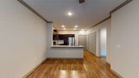 This single-floor unit offers a thoughtfully designed open-concept layout that seamlessly connects the kitchen and living area. The kitchen is a standout feature, showcasing rich dark-wood cabinetry with sleek hardware, light granite countertops, and a full suite of stainless steel appliances including a range, microwave, dishwasher, and refrigerator. A peninsula with an integrated sink provides additional prep space and creates a natural divide between the kitchen and the main living area. Recessed lighting and crown molding add a refined touch throughout the common areas. The living space features warm hardwood-style flooring that extends through the entryway and kitchen, contributing to a cohesive and inviting atmosphere. A ceiling fan overhead enhances comfort and airflow. The bedrooms are finished with plush wall-to-wall carpeting, neutral-toned walls, and ceiling fans, with natural light flowing in through windows with exterior views. The bathroom is appointed with granite countertops, an undermount sink, brushed nickel fixtures, and a large vanity mirror. Panel-style interior doors in a complementary gray tone provide a consistent, modern aesthetic throughout the unit.