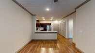 This single-floor unit offers a thoughtfully designed open-concept layout that seamlessly connects the kitchen and living area. The kitchen is a standout feature, showcasing rich dark-wood cabinetry with sleek hardware, light granite countertops, and a full suite of stainless steel appliances including a range, microwave, dishwasher, and refrigerator. A peninsula with an integrated sink provides additional prep space and creates a natural divide between the kitchen and the main living area. Recessed lighting and crown molding add a refined touch throughout the common areas. The living space features warm hardwood-style flooring that extends through the entryway and kitchen, contributing to a cohesive and inviting atmosphere. A ceiling fan overhead enhances comfort and airflow. The bedrooms are finished with plush wall-to-wall carpeting, neutral-toned walls, and ceiling fans, with natural light flowing in through windows with exterior views. The bathroom is appointed with granite countertops, an undermount sink, brushed nickel fixtures, and a large vanity mirror. Panel-style interior doors in a complementary gray tone provide a consistent, modern aesthetic throughout the unit.