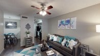 This two-floor residence offers a thoughtfully laid-out living experience with a cohesive design aesthetic throughout. The living room serves as the heart of the home, featuring dark hardwood-style flooring, a textured ceiling, and a ceiling fan with integrated lighting. The space flows naturally into the kitchen, which is equipped with dark espresso cabinetry, stainless steel appliances including a microwave and range, and a double basin sink with ample counter space. Track lighting overhead keeps the kitchen well-lit and functional. Adjacent to the kitchen, a cozy dining nook accommodates a four-seat table beneath a pendant light fixture, creating an intimate setting for meals. The bedroom is carpeted and includes a ceiling fan, a window that allows natural light to filter in, and access to a spacious walk-in closet with dual-level shelving and hanging rods. The bathroom is finished with a wide vanity topped in light countertop material, dark wood cabinetry below, a large mirror, and overhead globe lighting. Throughout the residence, neutral gray walls provide a versatile backdrop, and consistent design elements tie each room together into a comfortable, practical living space spanning two floors.