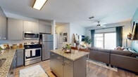 Located at 444 W College Ave in Tallahassee, FL, this 5-bedroom, 4-bathroom unit offers a well-designed single-floor layout with modern finishes throughout. The open-concept kitchen flows seamlessly into the living area and features gray flat-front cabinetry, granite countertops, a central island with bar seating, and a full suite of stainless steel appliances including a refrigerator, range, microwave, and dishwasher. Wood-style flooring runs throughout the main living areas, adding warmth and continuity to the space. The living room is bright and inviting, highlighted by a teal accent wall, a ceiling fan, and sliding glass doors that open onto a private balcony with outdoor views. Each of the five bedrooms is thoughtfully sized, offering natural light through sizable windows, wall-mounted televisions, and built-in study desks — ideal for focused work or study. Each bedroom is paired with a dedicated closet for added storage. The four bathrooms are finished consistently with granite-topped gray vanities, large mirrors, and wood-style flooring, maintaining a cohesive modern aesthetic. The overall ambiance is clean, contemporary, and functional, making this a well-appointed multi-bedroom unit suited for shared living.