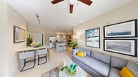 This single-floor residence offers a thoughtfully designed open-concept layout that maximizes its living space across three bedrooms and two bathrooms. Light-toned large-format tile flooring flows throughout, creating a cohesive and airy feel. The combined kitchen and living area serves as the heart of the home, anchored by a vaulted ceiling with a ceiling fan that enhances the sense of vertical space. The kitchen features contemporary flat-front cabinetry in a warm taupe finish, granite countertops, a tile backsplash, stainless steel appliances including a French-door refrigerator, dishwasher, and range, as well as a peninsula with bar seating illuminated by pendant lighting. Track lighting provides additional functional illumination. An in-unit stacked washer and dryer is conveniently integrated nearby. The living area accommodates comfortable seating and benefits from natural light. The primary bedroom provides a calm retreat with neutral tones and tile flooring. Both bathrooms are finished with granite vanity tops and modern cabinetry; one features a glass-enclosed walk-in shower, while the other offers a full soaking tub. Two closets provide practical storage throughout the residence.
