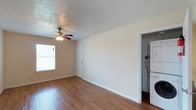 This single-floor unit offers a practical and comfortable layout with consistent warm-toned hardwood-style flooring running throughout the living areas and bedrooms. Ceiling fans are installed in each room, providing both light and airflow. The open living area features neutral wall tones, white trim baseboards, and a textured ceiling, creating a clean and inviting atmosphere. Natural light enters through windows fitted with blinds, brightening the space throughout the day.

The galley-style kitchen is well-appointed with rich medium-toned wood cabinetry, dark granite-style countertops, and white appliances including a stove, microwave, refrigerator, and dishwasher. The layout maximizes functionality with ample cabinet and counter space on both sides. A peninsula counter connects the kitchen to the living area, allowing for an open feel between the two spaces.

In-unit stacked washer and dryer are conveniently located just off the kitchen area, adding to the unit's practicality. The bedroom is generously sized with a walk-in closet offering valuable storage. The bathroom features a full tub-shower combination with a small window for natural light and ventilation, accompanied by a clean white finish throughout. Overall, this space is well-designed for comfortable everyday living.
