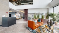 Located at 435 Main St in the heart of Hackensack, NJ, this thoughtfully designed lobby and amenity floor makes a striking first impression. The grand entrance features soaring double-height ceilings, floor-to-ceiling windows that flood the space with natural light, and expansive large-format tile flooring that flows seamlessly throughout. A standout textured brick column anchors the main lounge, where rich cognac leather sofas, vibrant patterned area rugs, and lush indoor plantings create a warm, inviting atmosphere. A bold, locally themed collage mural celebrates Hackensack's history, while a distinctive stacked wood accent wall bearing the city's name adds an authentic sense of place. A secondary lounge near the street-facing windows offers additional seating with eclectic accent chairs and abundant views of the surrounding neighborhood. The amenity wing features a well-appointed game room with exposed industrial ductwork, a billiards table, foosball, and a shuffleboard table set against teal accent walls and large windows overlooking an outdoor area. Patterned geometric tile flooring marks the elevator corridor, adding a refined touch to circulation spaces. Together, these areas deliver a cohesive blend of modern design, community-centered amenities, and local character.