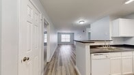 This single-floor, 2-bedroom, 2-bathroom residence offers a thoughtfully designed open-concept layout that maximizes its comfortable footprint. The combined kitchen and living area serves as the heart of the home, featuring warm wood-look luxury vinyl plank flooring that extends throughout the main living spaces. The kitchen is equipped with white cabinetry, dark granite-style countertops, a peninsula with a built-in sink, a dishwasher, and a refrigerator — all finished in a clean, bright aesthetic. The adjacent living area is generously proportioned, bathed in natural light from a large window overlooking the surrounding neighborhood.

The two bedrooms are carpeted for comfort and each feature windows that allow natural light to filter in. The spacious primary bedroom includes a closet and direct access to one of the two full bathrooms. Both bathrooms share a consistent design language, showcasing white vanities with undermount sinks, full tub-shower combinations, wood-look flooring, and large mirrors with overhead lighting. A hallway connects the private areas of the residence, and an additional closet provides convenient storage. The overall color palette of soft gray walls and crisp white trim creates a clean, neutral ambiance throughout.