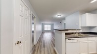 This single-floor, 2-bedroom, 2-bathroom residence offers a thoughtfully designed open-concept layout that maximizes its comfortable footprint. The combined kitchen and living area serves as the heart of the home, featuring warm wood-look luxury vinyl plank flooring that extends throughout the main living spaces. The kitchen is equipped with white cabinetry, dark granite-style countertops, a peninsula with a built-in sink, a dishwasher, and a refrigerator — all finished in a clean, bright aesthetic. The adjacent living area is generously proportioned, bathed in natural light from a large window overlooking the surrounding neighborhood.

The two bedrooms are carpeted for comfort and each feature windows that allow natural light to filter in. The spacious primary bedroom includes a closet and direct access to one of the two full bathrooms. Both bathrooms share a consistent design language, showcasing white vanities with undermount sinks, full tub-shower combinations, wood-look flooring, and large mirrors with overhead lighting. A hallway connects the private areas of the residence, and an additional closet provides convenient storage. The overall color palette of soft gray walls and crisp white trim creates a clean, neutral ambiance throughout.