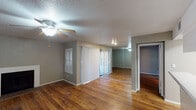 This single-floor residence is defined by rich, warm-toned hardwood flooring that runs consistently throughout the entire space, lending a cohesive and inviting character to every room. The main living area is anchored by a classic fireplace with a clean white surround, complemented by a ceiling fan overhead and a textured ceiling. Vertical blinds on sliding glass doors allow for controlled natural light and easy access to the outdoors. A pass-through peninsula connects the living area to the galley-style kitchen, which is well-equipped with white cabinetry, ample counter space, a double stainless steel sink, and full-size appliances including a refrigerator and dishwasher. A narrow window provides ventilation and a touch of natural light to the kitchen. A mirrored wall accent in the living and dining area adds depth and brightness to the open layout. The bedrooms are generously sized, each featuring vertical-blind-covered windows that draw in natural light and neutral-toned walls that create a calm atmosphere. One bedroom includes direct access to a walk-in closet and a private full bathroom complete with a tub and shower. Throughout the space, the consistent use of neutral gray and taupe wall tones, white trim, and hardwood flooring creates a unified, functional, and comfortable living environment.
