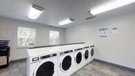 Located at 2414 Timbertrail Dr S in Columbus, Ohio, this single-floor community laundry facility is designed with functionality and convenience in mind. The room is outfitted with a row of commercial-grade Maytag front-loading washers and dryers, providing ample capacity to serve multiple users efficiently. A continuous countertop runs along the top of the machines, offering a practical surface for sorting and folding laundry. The space is finished with neutral gray walls and a durable tile floor, contributing to a clean and easy-to-maintain environment. Bright fluorescent ceiling fixtures ensure thorough, even illumination throughout the room, making it comfortable to use at any hour. Natural light also filters in through multiple windows fitted with blinds, adding to the welcoming atmosphere. Ventilation is addressed through ceiling vents, supporting a fresh and comfortable interior. Instructional signage is posted on the wall, providing users with clear guidance on proper machine use. Overall, the facility presents a tidy, well-organized space that prioritizes practicality and ease of use for its residents.