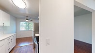 This efficient and thoughtfully laid-out one-bedroom, one-bathroom unit spans a single floor and offers a clean, modern aesthetic throughout. The living room features rich hardwood-style flooring, white walls, and a sliding glass door fitted with vertical blinds that opens to a view of lush greenery, providing an abundance of natural light and a seamless indoor-outdoor feel. The kitchen is stylishly updated with white shaker cabinetry accented by matte black hardware, a white subway tile backsplash, light countertops, a stainless steel refrigerator, a black electric range, and a stainless sink. A ceiling fan with a light fixture adds both function and character to the kitchen and adjacent dining space, which also benefits from a large window overlooking treed surroundings. The hallway connects the main living areas to the bedroom and bathroom, and also houses a stacked washer and dryer unit for added convenience. The generously sized bedroom is finished with plush carpet, a textured ceiling, a window with blinds, and a mirrored sliding closet door. The bathroom is neatly appointed with a white vanity, matte black fixtures, a framed mirror, and hardwood-style flooring that ties back to the rest of the unit's cohesive design.
