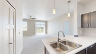 Located at 5005 Verdure Pkwy SE in Grand Rapids, Michigan, this well-appointed 2-bedroom, 2-bathroom residence offers a thoughtfully designed single-floor layout. The open-concept kitchen and living area serves as the heart of the home, where pendant lighting highlights a large kitchen island with a double stainless steel sink. The kitchen features rich, dark wood-toned cabinetry, light quartz-style countertops, and a full suite of stainless steel appliances including a gas range, microwave, and refrigerator, complemented by wood-look luxury vinyl flooring. The living area flows seamlessly from the kitchen and is bathed in natural light from a sliding glass patio door and additional windows, with a ceiling fan overhead adding comfort. Both bedrooms offer plush carpeting, ceiling fans, and ample natural light. The spacious primary bedroom includes its own sliding glass door, bringing in an abundance of daylight and outdoor views. Each bathroom is finished with dark wood vanities, light countertops, and wood-look flooring; one features a backlit vanity mirror and walk-in shower, while the other includes a full tub-shower combination. A dedicated closet provides practical storage. The overall ambiance is clean, modern, and move-in ready.