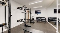 Located at 4603 Minnehaha Ave in Minneapolis, MN, this single-level fitness facility offers a thoughtfully designed workout environment spread across three distinct zones. The space is finished with crisp white walls and consistent recessed and linear LED lighting throughout, creating a bright, clean, and energizing atmosphere.

The cardio area features rubber flooring and houses a lineup of machines including treadmills, stationary bikes, a rowing machine, and elliptical trainers, all arranged along the perimeter for ease of movement. A wall-mounted television adds to the workout experience. Vibrant artwork along the walls adds a touch of character to the space.

The strength training room is outfitted with professional-grade Rogue equipment, including a wall-mounted power rack with cable attachments and gymnastic rings, a flat bench, and a full dumbbell rack. Rubber flooring provides safety and durability underfoot, while a wall-mounted display screen keeps users engaged.

A flexible open workout room features light hardwood-style flooring, floor-to-ceiling mirrors that visually expand the space, and ample room for stretching, yoga, or bodyweight exercises. Yoga mats, balance tools, and a stability ball are available within this area.

A connecting corridor with built-in storage shelving ties the zones together, giving the facility a cohesive and functional flow suited for diverse fitness needs.