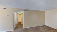 Located at 145-149 Canyon in Oceanside, this single-story unit offers a straightforward, functional layout finished throughout in warm neutral tones. The living area is generously proportioned, featuring wall-to-wall carpeting, textured ceilings, and a large sliding glass door dressed with vertical blinds that allows natural light to fill the room. The entry foyer transitions from wood-look flooring into the carpeted living space, providing a clear sense of arrival.

The kitchen is equipped with white cabinetry, a gas range, and a full-size refrigerator, with wood-look flooring that extends through the space. A countertop bar area connects the kitchen to the adjacent living zone, creating an open and accessible flow between the two areas.

The bedroom continues the carpeted flooring and neutral palette, featuring a sliding double-door closet with a hanging rod for organized storage. A ceiling light fixture adds practical illumination to the room.

The bathroom includes a full tub and shower combination with chrome fixtures, a single-sink vanity with a light-toned countertop, and a large mirror above. Wood-look flooring completes the space. Overall, the unit presents a clean, move-in ready environment with consistent finishes throughout.