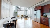 Located in the heart of uptown Charlotte at 215 N Pine Street, this two-story loft offers a striking blend of modern industrial design and refined urban living. The main level welcomes you with soaring double-height ceilings, expansive floor-to-ceiling windows, and warm hardwood flooring that runs throughout. Exposed ductwork adds an industrial character, while the open-plan layout seamlessly connects the living, dining, and kitchen areas. The living room is bathed in natural light and opens to a balcony with sweeping panoramic views of the Charlotte skyline and surrounding cityscape. A sculptural spiral staircase serves as both a functional and architectural centerpiece, connecting the two levels. The kitchen is well-appointed with rich dark wood cabinetry, granite countertops, a glass tile backsplash, and a full suite of stainless steel appliances. Upstairs, the bedroom loft overlooks the main living area through an open railing and is framed by large windows that continue the stunning city views. The upper level features polished dark hardwood floors and ceiling fans. Bathrooms are finished with tile surrounds, granite vanities, and wood cabinetry. A clean, minimalist half-bath with light tile flooring completes the layout. This residence offers an exceptional elevated urban living experience in one of Charlotte's most sought-after locations.