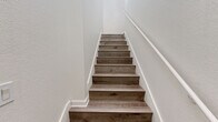 Located on Fenton Parkway in San Diego's Mission Valley area (92108), this two-story, one-bedroom, one-bathroom home is thoughtfully laid out across two levels. The ground floor houses a private garage with tile flooring, an automatic opener, and exposed beam ceiling details. A staircase connects to the main living level above, which comprises the majority of the home's total floor area.

The main level features light hardwood-style flooring throughout and is bathed in natural light from multiple windows, including a charming arched window and a set of French doors that open to an outdoor view. High ceilings in the living area enhance the sense of openness, complemented by a ceiling fan with light fixture.

The kitchen is well-appointed with white shaker-style cabinetry, granite-look countertops, and a full suite of stainless steel appliances including a gas range, microwave, dishwasher, and refrigerator. A sliding glass door in the kitchen area provides additional natural light and outdoor access.

The spacious primary bedroom features vaulted ceilings, a ceiling fan, and leads to a generous walk-in closet outfitted with built-in shelving and hanging rods. The bathroom is finished with a white vanity, granite-look countertop, and a full tub-shower combination.
