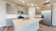 This two-story home offers a thoughtfully designed layout across two floors, combining modern aesthetics with functional living spaces. The main floor features an open-concept kitchen and living area bathed in natural light from multiple windows. The kitchen is a standout, boasting a large quartz-topped island with an undermount sink, gray shaker-style cabinetry, a white subway tile backsplash, stainless steel appliances, and globe pendant lights that add a contemporary touch. The living area continues the light and airy feel with wood-look flooring, a ceiling fan, and several windows that bring in abundant natural light.

A staircase connects to the upper floor, where both bedrooms are located. Each bedroom features plush carpet flooring, ceiling fans, and windows that provide natural light. The spacious primary bedroom offers a comfortable retreat with a well-sized walk-in closet and an en-suite bathroom. The bathrooms are finished with gray vanity cabinetry, white countertops, and wood-look tile flooring. Three closets throughout the home provide ample storage. Clean neutral walls, consistent trim work, and a cohesive modern palette tie the entire home together, creating a fresh and inviting atmosphere throughout.