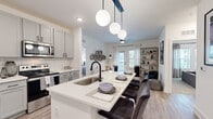 This well-appointed single-floor residence combines modern design with functional living across a thoughtfully arranged floor plan. The open-concept kitchen is a standout feature, outfitted with soft gray shaker-style cabinetry, white quartz countertops, a classic subway tile backsplash, and a full suite of stainless steel appliances including a French door refrigerator, electric range, microwave, and dishwasher. A large center island with a deep undermount sink and seating for multiple bar-height chairs serves as the heart of the space, anchored above by a striking trio of globe pendant lights on a matte black fixture. The kitchen flows seamlessly into the living area, where light wood-look flooring, neutral walls, and a sliding glass door leading to a private balcony create a bright and airy atmosphere. The primary bedroom features plush carpet, natural light from a large window, and a spacious walk-in closet with wire shelving and hanging rods. A second bedroom offers similar comfort with floating wall shelves and soft, neutral tones. The bathroom is finished with gray vanity cabinetry, a white quartz countertop, a large framed mirror, and light wood-look flooring, continuing the cohesive modern aesthetic found throughout the residence.