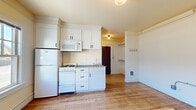 Located at 2631 N Mississippi Ave in Portland's vibrant Mississippi Avenue corridor, this single-floor studio unit offers a thoughtfully utilized layout with a warm, classic character. Hardwood flooring runs throughout the open living area, lending a sense of continuity and timeless charm. The kitchen is efficiently designed with white cabinetry extending to the ceiling, a gas range, refrigerator, microwave, and a stainless steel sink, making the most of the available space. Large windows in the kitchen area invite abundant natural light and provide street views, brightening the interior considerably. The open main living area features clean white walls, built-in coat hooks, and exposed conduit details that add a functional, utilitarian touch. A separate window in the living space further enhances natural light. The bathroom retains its vintage character with classic white subway tile surrounding a soaking tub and shower combination, a pedestal sink, a medicine cabinet mirror, and distinctive black-and-white hexagonal mosaic tile flooring. Crown molding details and globe light fixtures contribute to the unit's period-appropriate aesthetic. Overall, the space presents a clean, bright, and functional environment with a charming old-Portland character.