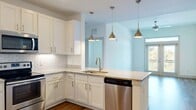 Located at 4450 Tropea Way in Jacksonville, Florida, this single-floor residence offers a well-designed layout with modern finishes throughout. The open-concept kitchen is a standout feature, showcasing crisp white shaker cabinetry, granite countertops, a classic subway tile backsplash, and stainless steel appliances including a range and dishwasher. A peninsula with pendant lighting in brushed gold adds both function and style, while the space flows seamlessly into the main living area. The living room is bathed in natural light from a set of French doors topped with a transom window, opening to a private balcony with pleasant outdoor views of lush greenery. Hardwood-style flooring runs throughout the main living areas, complementing the light, neutral color palette. The bathroom features a dual-sink vanity with granite countertops, a large mirror, and a walk-in glass-enclosed shower with tile surround. Bedrooms are carpeted for comfort and include generous closet space, with one room offering a walk-in closet fitted with wire shelving. A dedicated laundry closet with louvered doors provides added convenience. The overall ambiance is clean, bright, and move-in ready.