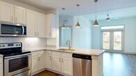 Located at 4450 Tropea Way in Jacksonville, Florida, this single-floor residence offers a well-designed layout with modern finishes throughout. The open-concept kitchen is a standout feature, showcasing crisp white shaker cabinetry, granite countertops, a classic subway tile backsplash, and stainless steel appliances including a range and dishwasher. A peninsula with pendant lighting in brushed gold adds both function and style, while the space flows seamlessly into the main living area. The living room is bathed in natural light from a set of French doors topped with a transom window, opening to a private balcony with pleasant outdoor views of lush greenery. Hardwood-style flooring runs throughout the main living areas, complementing the light, neutral color palette. The bathroom features a dual-sink vanity with granite countertops, a large mirror, and a walk-in glass-enclosed shower with tile surround. Bedrooms are carpeted for comfort and include generous closet space, with one room offering a walk-in closet fitted with wire shelving. A dedicated laundry closet with louvered doors provides added convenience. The overall ambiance is clean, bright, and move-in ready.
