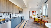 Located on East Fourth Street in the heart of downtown Cleveland, this modern studio residence offers a thoughtfully designed open-concept layout that seamlessly integrates the kitchen, living, and sleeping areas into one cohesive living space. Wide-plank hardwood-style flooring runs throughout, tying the interior together with a warm yet contemporary feel.

The kitchen is a standout feature, outfitted with sleek slate-blue lower cabinetry, warm wood-toned upper cabinets, and a striking geometric-patterned tile backsplash. Dark countertops, a matte black faucet, and a full suite of stainless steel appliances — including a refrigerator, dishwasher, range, and microwave — complete this well-appointed cooking space.

The sleeping area benefits from large, black-framed industrial-style windows that frame impressive views of the Cleveland skyline, filling the space with natural light. A walk-in closet provides generous storage, while colorful contemporary artwork adds personality throughout.

The bathroom features crisp white subway tile surrounding a soaking tub and shower, hexagonal floor tile in charcoal, matte black fixtures, and a wood-textured vanity with a clean white countertop — balancing modern and industrial aesthetics with everyday functionality.
