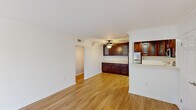 This single-floor, 1-bedroom, 1-bathroom residence offers a practical and comfortable layout across a compact yet efficient footprint. The open-concept living and kitchen area serves as the heart of the unit, featuring warm hardwood-style flooring, crown molding, and a ceiling fan with light fixture that enhances airflow and ambiance. The kitchen is outfitted with rich dark wood cabinetry—including upper glass-paneled cabinets and generous lower storage—complemented by stainless steel appliances including a refrigerator, gas range, and microwave. A peninsula-style counter separates the kitchen from the living area, adding both function and definition to the space. The living room benefits from a sliding glass door and a front entry door with a sidelight window, allowing natural light to fill the room and providing access to the outdoors. The bedroom is a comfortable size, finished with plush carpeting and a window that brings in natural light, along with a dedicated closet for storage. The bathroom is thoughtfully designed with accessibility in mind, featuring grab bars around a full tub and shower, a toilet, and a vanity with a stone-topped counter and dark wood cabinetry. A hallway connects the main living areas to the private spaces, contributing to a well-organized and functional floor plan throughout.