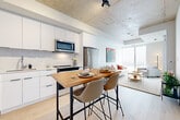 Located at 300 Mìwàte Pvt in Ottawa, this thoughtfully designed one-bedroom, one-bathroom unit offers a compact yet highly functional layout across a single floor. The open-concept kitchen and living area serves as the heart of the space, featuring a modern white cabinetry kitchen with marble-style backsplash, stainless steel appliances including a dishwasher, and a wood-top bar-height dining table. Striking exposed concrete ceilings and light hardwood flooring run throughout, lending an industrial-modern aesthetic. The living area is bathed in natural light from expansive floor-to-ceiling windows that frame city views, with access to an outdoor balcony. Track lighting on the concrete ceiling adds a contemporary touch. The bedroom is a calm, minimalist retreat with a built-in sliding closet and clean white walls. A dedicated office nook provides a quiet space for focused work. The bathroom is finished with large-format grey wall tiles surrounding the soaker tub, a white floating vanity, and light tile flooring. A hallway connects all rooms efficiently, completing this well-appointed urban residence.