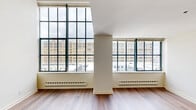 Located at 317 North Broad Street in the heart of Philadelphia, this two-story, one-bedroom, two-bathroom residence offers a thoughtfully designed layout spread across two levels. The main floor opens through a hallway into a spacious living area distinguished by dramatic floor-to-ceiling steel-framed windows that flood the space with natural light and frame sweeping views of the Philadelphia skyline. Hardwood flooring runs throughout the living area, complementing the bright, neutral palette of the walls. The kitchen features rich cherry wood cabinetry, dark granite countertops, tile flooring, and a full suite of stainless steel appliances, including a range, microwave, dishwasher, and refrigerator. A convenient pass-through connects the kitchen to the living area. The main level also includes a bathroom with a granite vanity countertop and a large mirror. A staircase leads to the upper level, where the primary bedroom offers plush carpeting, a large window with urban views, tall ceilings, and direct access to a private en-suite bathroom. A second, smaller carpeted room on the upper level provides added flexibility. The residence combines industrial architectural character with modern finishes throughout.