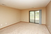 This single-floor unit offers a practical and functional layout designed for comfortable everyday living. The galley-style kitchen is efficiently organized, featuring white cabinetry with light wood trim, light-colored countertops, and a full suite of black appliances including an electric range, built-in microwave, refrigerator, and dishwasher. Light wood-look flooring runs throughout the kitchen, adding warmth to the space.

The bathroom is notably multifunctional, incorporating a stacked washer and dryer unit within a dedicated closet alcove, alongside a soaking tub, vanity with countertop sink, and a towel bar. The same wood-look flooring continues here, complementing the neutral beige tones of the walls.

The bedroom is a well-proportioned, carpeted room equipped with a ceiling fan and light fixture, and features a window overlooking outdoor greenery, allowing for natural light.

The living area is spacious and carpeted, with warm neutral wall tones and two-tone grey and beige accent walls. A sliding glass door provides direct access to an outdoor patio, filling the room with natural light. The front entry opens directly into this living space, which connects openly to the kitchen, creating a cohesive and accessible floor plan throughout.