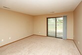 This single-floor unit offers a practical and functional layout designed for comfortable everyday living. The galley-style kitchen is efficiently organized, featuring white cabinetry with light wood trim, light-colored countertops, and a full suite of black appliances including an electric range, built-in microwave, refrigerator, and dishwasher. Light wood-look flooring runs throughout the kitchen, adding warmth to the space.

The bathroom is notably multifunctional, incorporating a stacked washer and dryer unit within a dedicated closet alcove, alongside a soaking tub, vanity with countertop sink, and a towel bar. The same wood-look flooring continues here, complementing the neutral beige tones of the walls.

The bedroom is a well-proportioned, carpeted room equipped with a ceiling fan and light fixture, and features a window overlooking outdoor greenery, allowing for natural light.

The living area is spacious and carpeted, with warm neutral wall tones and two-tone grey and beige accent walls. A sliding glass door provides direct access to an outdoor patio, filling the room with natural light. The front entry opens directly into this living space, which connects openly to the kitchen, creating a cohesive and accessible floor plan throughout.