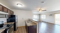 Located at 3410 5th Ave NE in Watford City, North Dakota, this single-floor, 2-bedroom, 2-bathroom unit offers a well-organized and functional layout. The open-concept kitchen and living area serve as the heart of the home, featuring dark espresso cabinetry, granite-style countertops, stainless steel appliances including a range, microwave, and refrigerator, and a peninsula with a double sink that overlooks the living room. Wood-style flooring runs throughout the main living areas, complemented by a ceiling fan and windows that bring in natural light and neighborhood views.

The living room offers access to a sliding door with vertical blinds and includes a wall-mounted air conditioning unit for added comfort, alongside baseboard heating. Both bedrooms are carpeted and feature ceiling fans and ample closet space, with the spacious primary bedroom offering double closets. Each bathroom is appointed with dark wood vanities, white countertops, and well-lit mirrors. A dedicated laundry room houses a full-size washer and dryer with a built-in overhead shelf for storage. Neutral tones and wood-trimmed doors and windows create a cohesive, clean aesthetic throughout the unit.